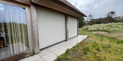 Hoek van een huis met grote ramen bedekt door screens, omgeven door wild gras Hoek van een huis met grote ramen bedekt door screens, omgeven door wild gras