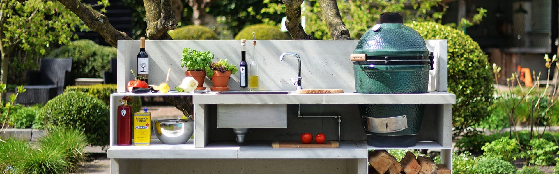 Buitenkeuken met groene keramische barbecue, kruidenplanten en kookbenodigdheden