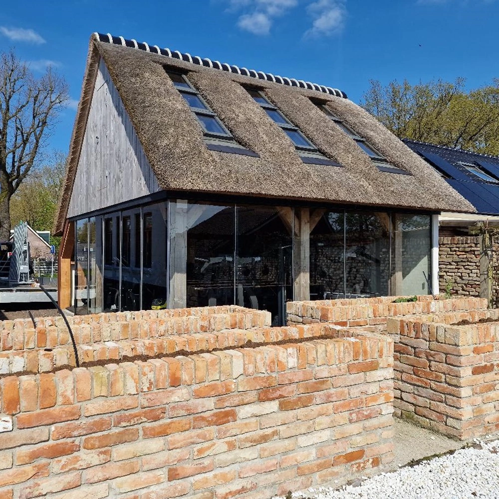 Buitenverblijf met rieten dak glazen schuifwanden en bakstenen omheining