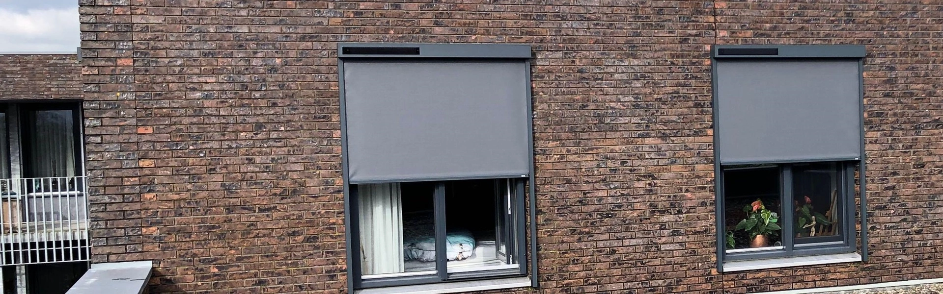 Grijze screens op bakstenen gevel met openslaande ramen en planten