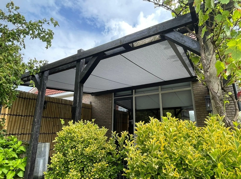 Serrezonwering met zwart houten frame en strak doek in groene tuin